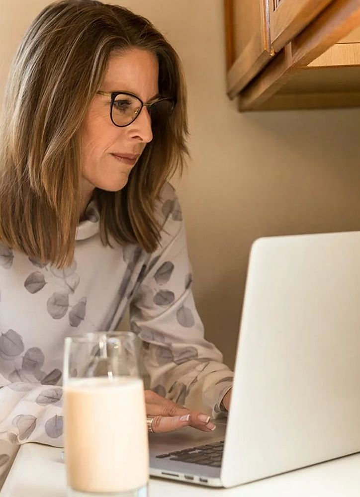 Woman using her computer in the kitchen counter drinking a glass of milk